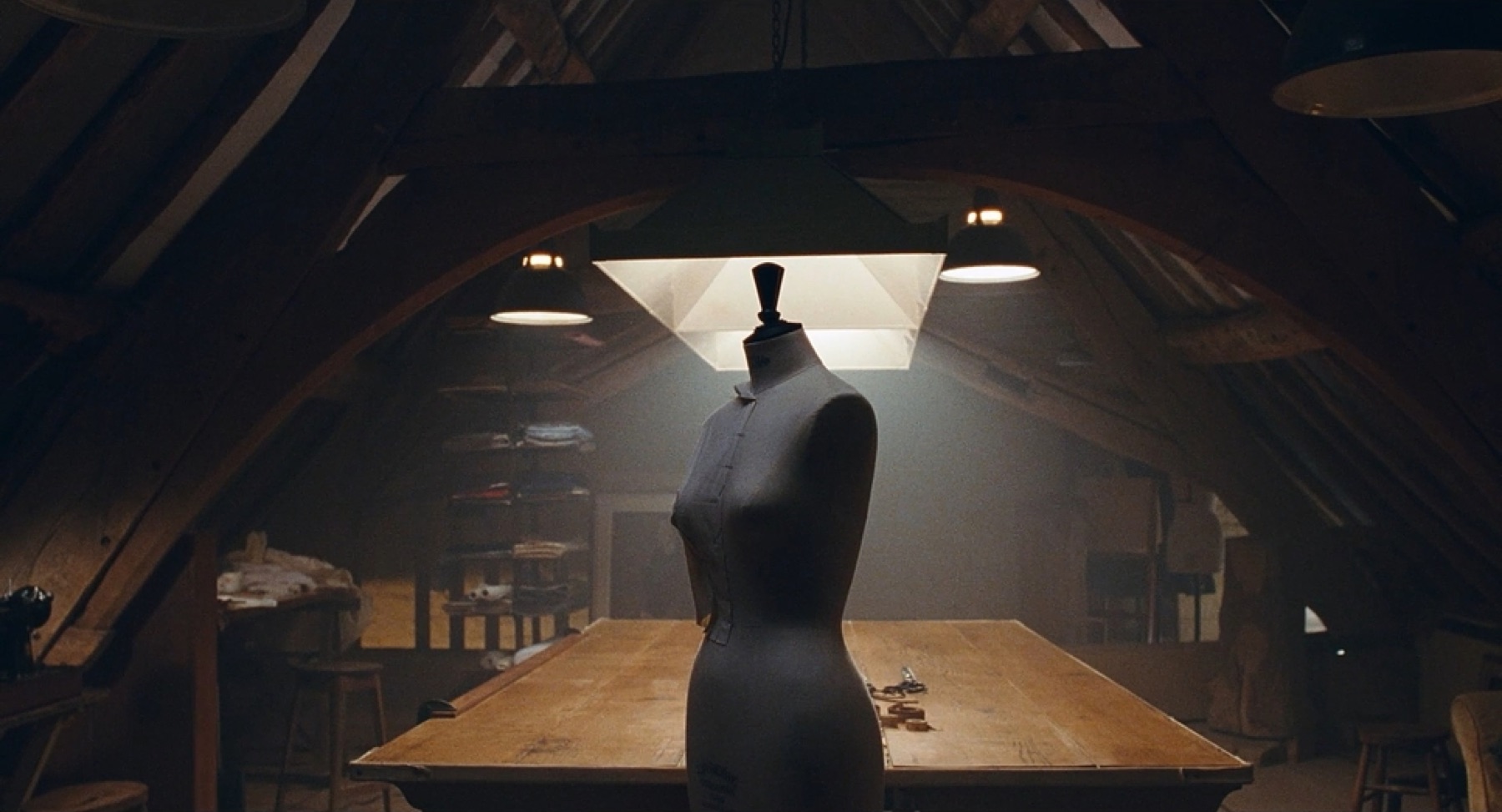 A dress form under a hanging lamp in a dim attic workshop