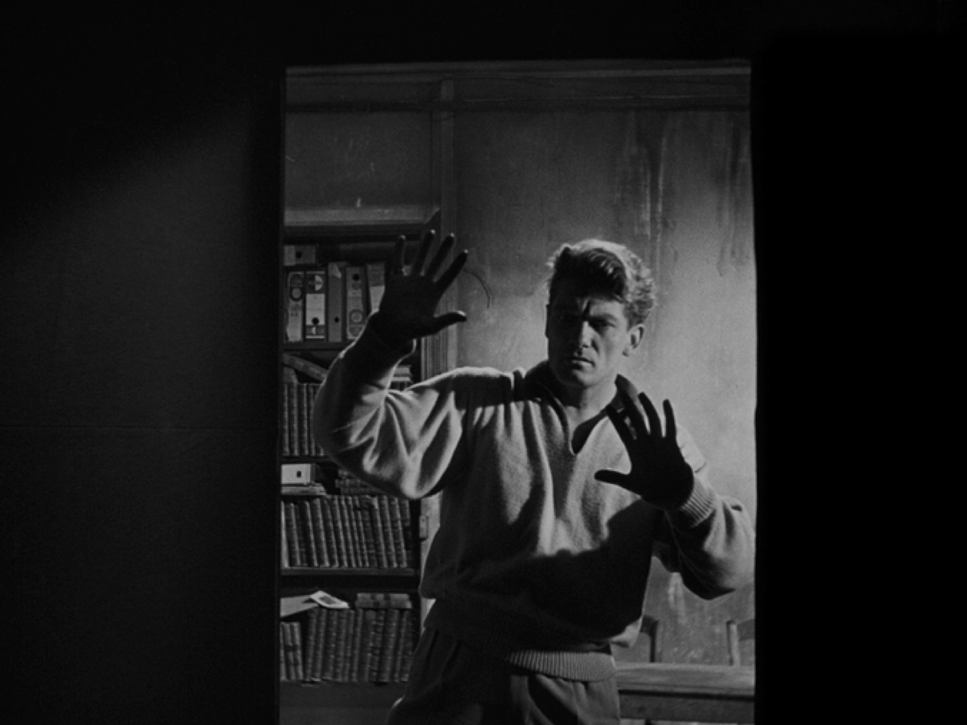 Black and white portrait of a man raising a gloved hand in a study